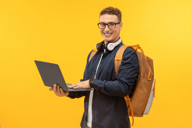 istock Happy young man student using laptop on yellow background 1995892280