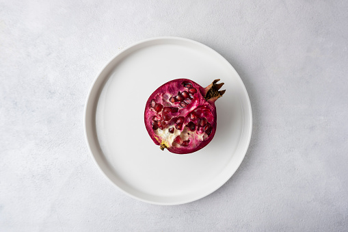 Opened ripe pomegranate on a white plate, top view of a ripe pomegranate. Concept of cleaning pomegranate bunches. Southern fruits.