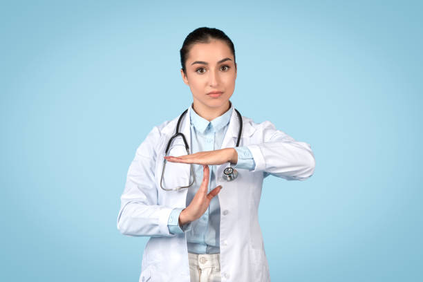 istock Confident woman doctor in white coat with stethoscope doing time out gesture with hands, blue studio background 1995923150
