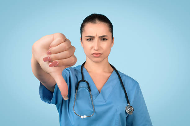istock Sad female nurse with thumbs down on blue background 1995923709