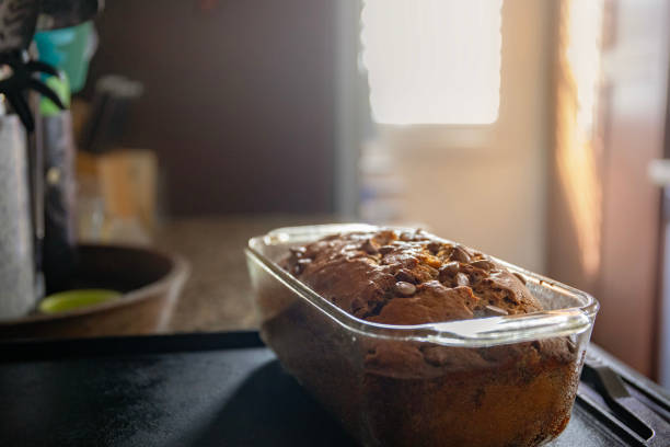 Freshly baked banana bread with chocolate chips sitting on a counter cooling off as the sun shines behind it through a window.