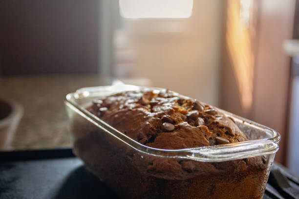 Freshly baked banana bread with chocolate chips sitting on a counter cooling off as the sun shines behind it through a window.