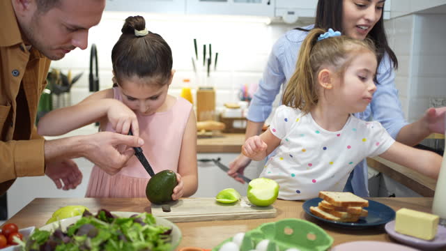Caucasian family, parents with daughters making healthy breakfast together , daughter is trying to use a knife