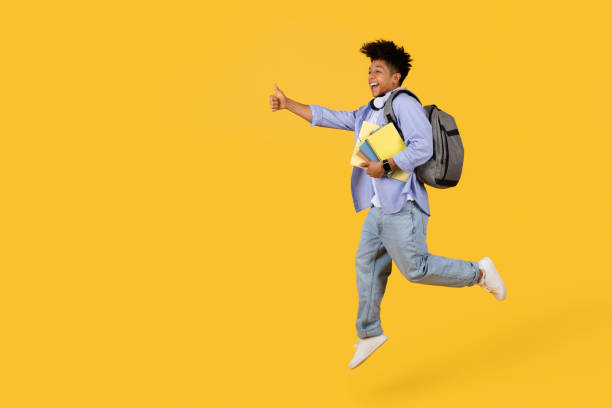 istock Joyful black student guy jumping with thumb up, free space on yellow background 1995947883