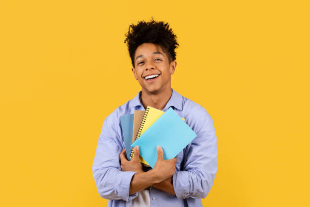 istock Content black male student hugging notebooks on yellow backdrop 1995947915