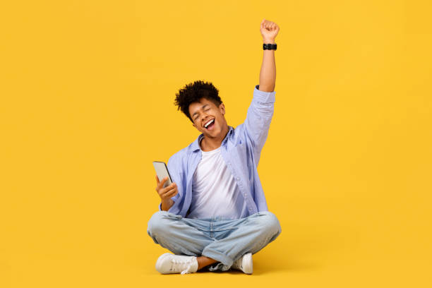 Happy student with smartphone celebrating success on yellow background stock photo