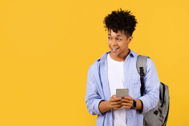 istock Happy black male student texting on phone with backpack on yellow 1995948458