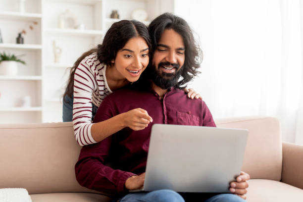 istock Loving cheerful indian couple using laptop together, cozy home interior 1995961554