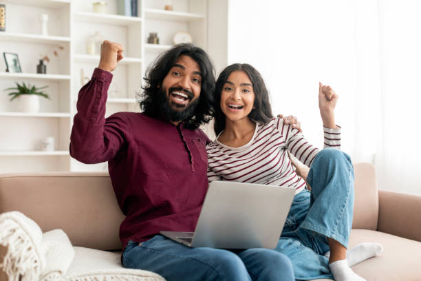 istock Emotional indian couple sitting on couch at home, using laptop 1995962093