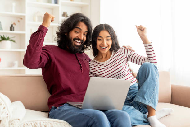 istock Excited happy beautiful indian couple using laptop 1995963226