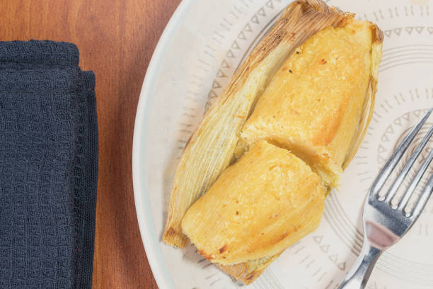 istock Top view of a ¨Envuelto de Mazorca¨ split in two on a corn husk and a fork on a plate. Delicious Colombian food made from corn. Wrapped corn on the cob 1995973007