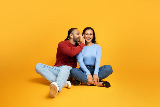 istock Man sharing secrets with girlfriend, millennial couple on yellow 1995979764