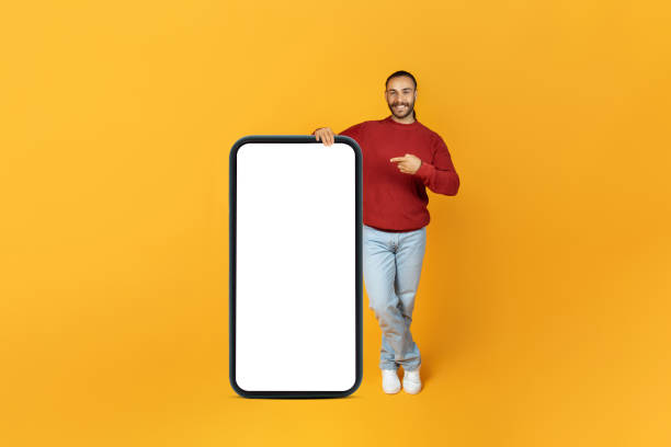 istock Cheerful millennial man pointing at big smartphone, mockup 1995979771