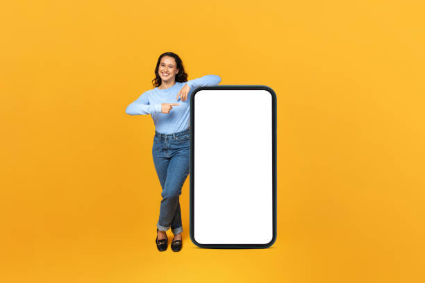 istock Cheerful millennial lady showing huge phone with blank screen 1995979772