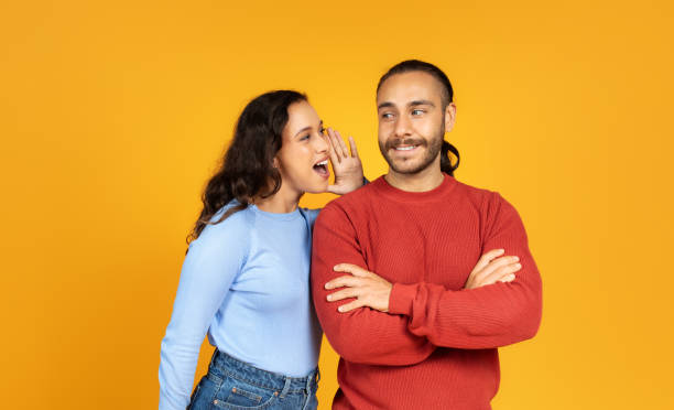 istock Young woman sharing secret with her husband, yellow background 1995980834