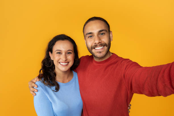 istock Cute positive young couple taking selfie on yellow background 1995980852