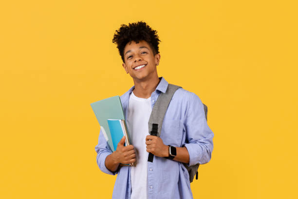 istock Cheerful black male student with books and backpack on yellow background 1995982408