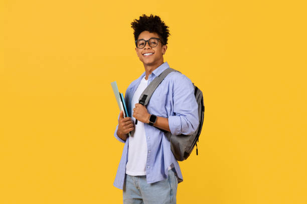 istock Happy black male student with glasses and backpack on yellow background 1995982413