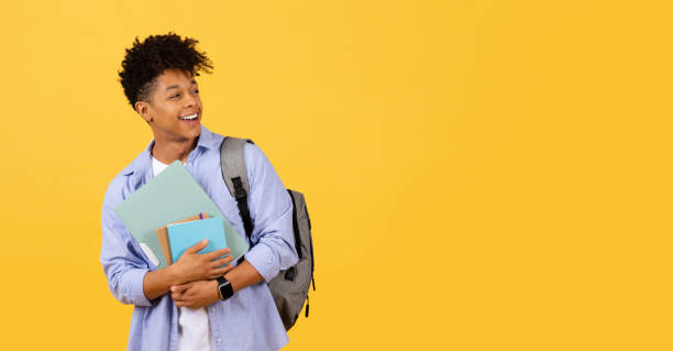 istock Joyful black student with books and backpack on yellow 1995982414