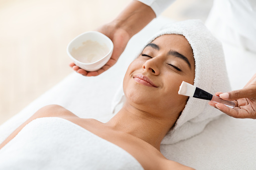 Skin Lifting Treatment. Young indian woman getting facial nourishing mask by professional beautician at spa salon, calm lady enjoying wellness day and beauty procedures, copy space