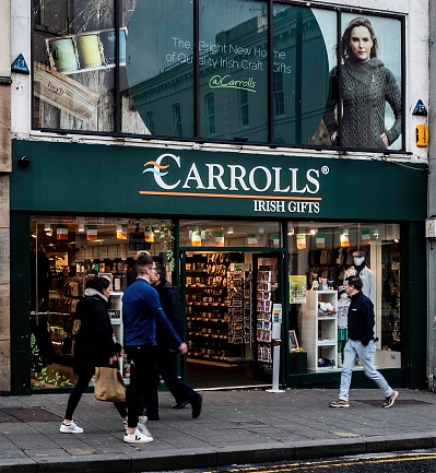People stride by the popular Carrolls Irish Gifts store, in Galway, Ireland, showcasing a variety of traditional Irish crafts and souvenirs.