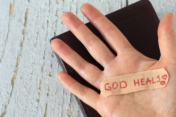 hand with handwritten quote "god heals" on a bandage on top of holy bible book - jesus christ human hand god consoling imagens e fotografias de stock