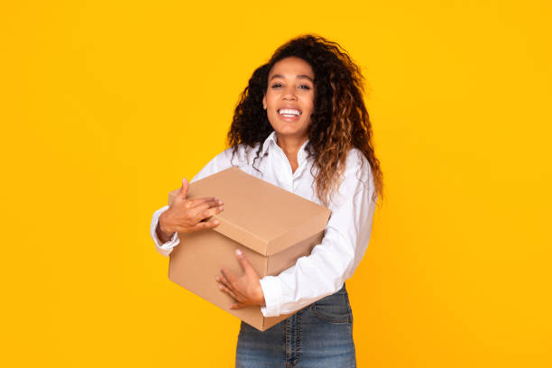 istock Cheerful Black Lady Holding Parcel Box On Yellow Studio Background 1996049451