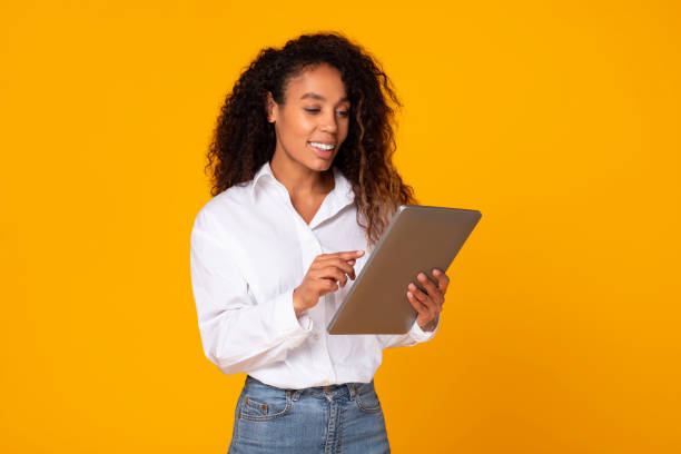 istock Happy young black woman using tablet computer over yellow background 1996049975