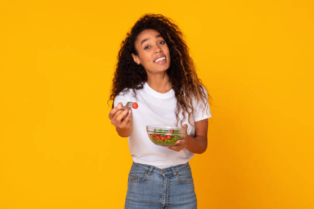 istock black woman with vegetable salad offering fork to you, studio 1996050507