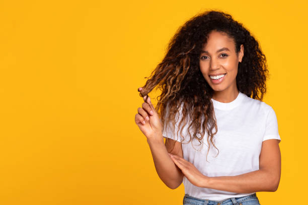 istock Black young lady twirls her curly hair against yellow backdrop 1996050521