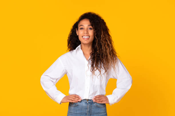 istock Black millennial lady standing holding hands on hips, yellow backdrop 1996050946