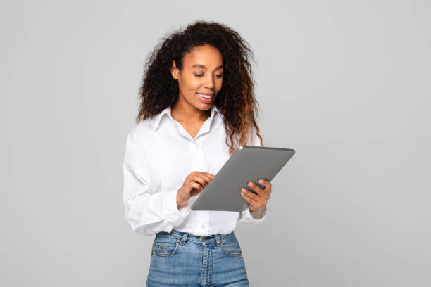 istock Happy young black woman engaging with digital tablet, gray background 1996051085