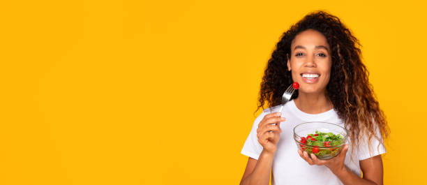 istock Black lady holding fresh salad in bowl on yellow background 1996051105