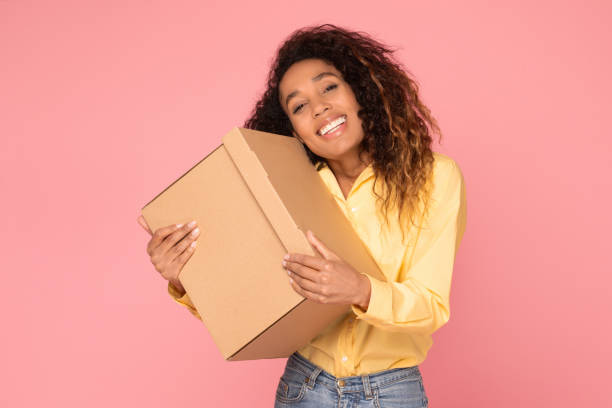 istock Joyful black lady holding a cardboard box, pink background, mockup 1996067226