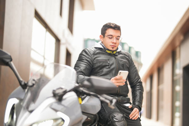istock Young man sitting on racing motorcycle and looking at his mobile phone 1996086874