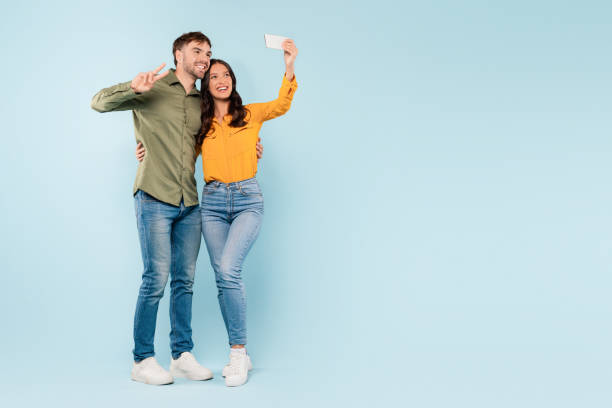 Happy couple taking selfie with peace sign on blue background