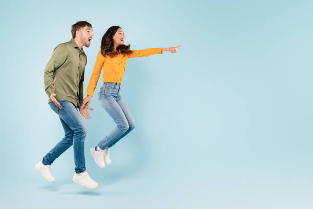 istock Excited couple jumping and pointing at free space on blue background 1996094566