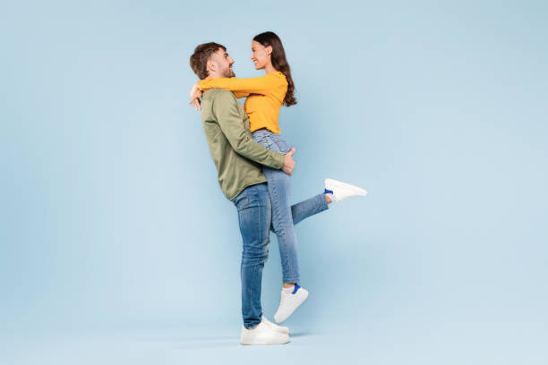 istock Man lifting woman in joyful hug on blue backdrop, full length 1996094571