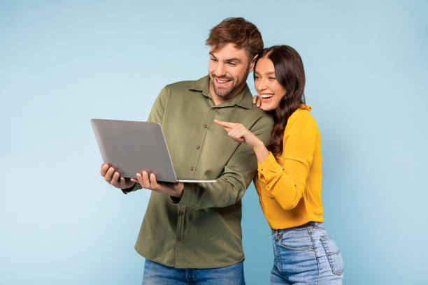 istock Couple with laptop smiling and pointing at screen on blue background 1996094574