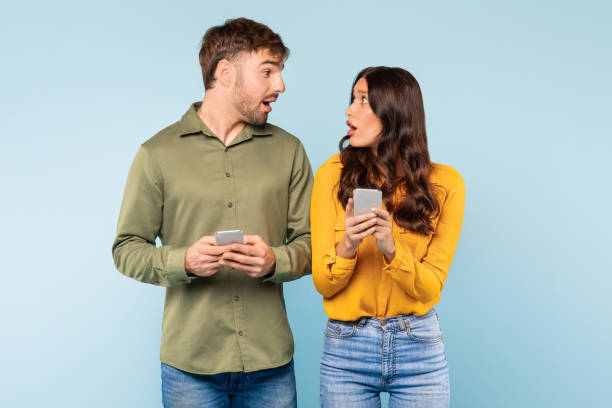 istock Surprised couple with smartphones on blue background 1996094586