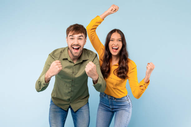 istock Ecstatic couple celebrating success with fists raised, blue background 1996095136