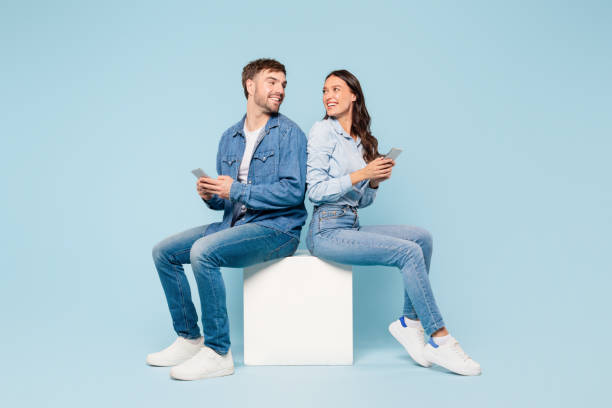 istock Casual couple in denim smiling and using smartphones back to back 1996095140