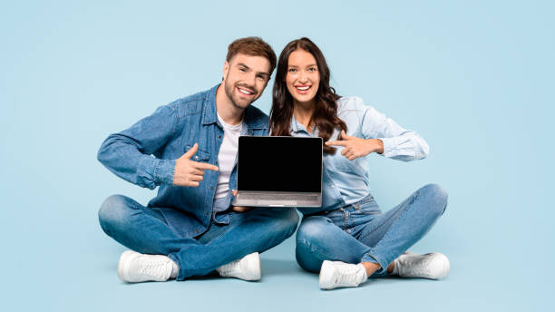 istock Smiling duo in denim with laptop, pointing at screen 1996095662