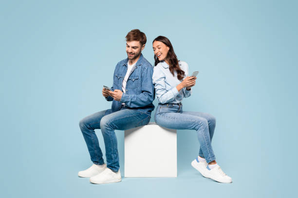 Couple in denim on cube using phones, back-to-back