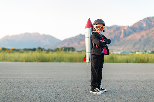 A young boy and businessman is dressed in a business suit with a homemade rocket strapped to his back. He is ready to use his smarts to launch his business to the next level. Taken in Utah, USA.