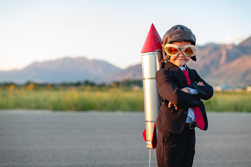 A young boy and businessman is dressed in a business suit with a homemade rocket strapped to his back. He is ready to use his smarts to launch his business to the next level. Taken in Utah, USA.
