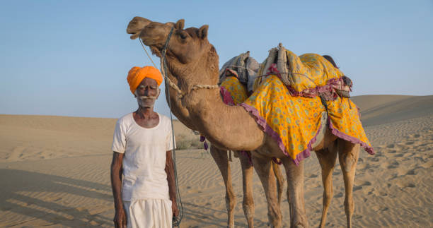 istock Indian man posing with camels on sand dunes, Rajasthan, India 1996173505