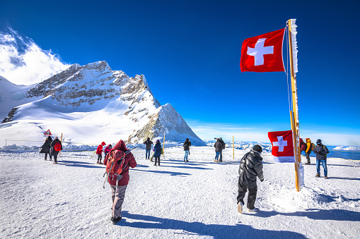 Tourists in front of Swiss flag on Jungfraujoch peak, Berner Oberland region of Switzerland