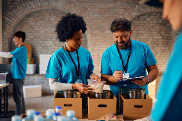 istock Volunteers cooperating while sorting donated food into cardboard boxes at charitable foundation. 1996181187