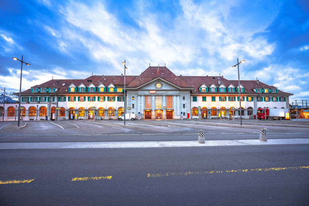 This panoramic view showcases the iconic Mittlere Rheinbrücke in Basel, Switzerland, a historic bridge crossing the Rhine River. The vibrant green tram traverses the bridge, blending seamlessly with the classic European architecture and modern high-rises in the background. The tranquil river and the charming cityscape make this a picturesque representation of Basel’s unique fusion of history, culture, and modernity. This central location serves as a hub of activity and a significant landmark in the region.